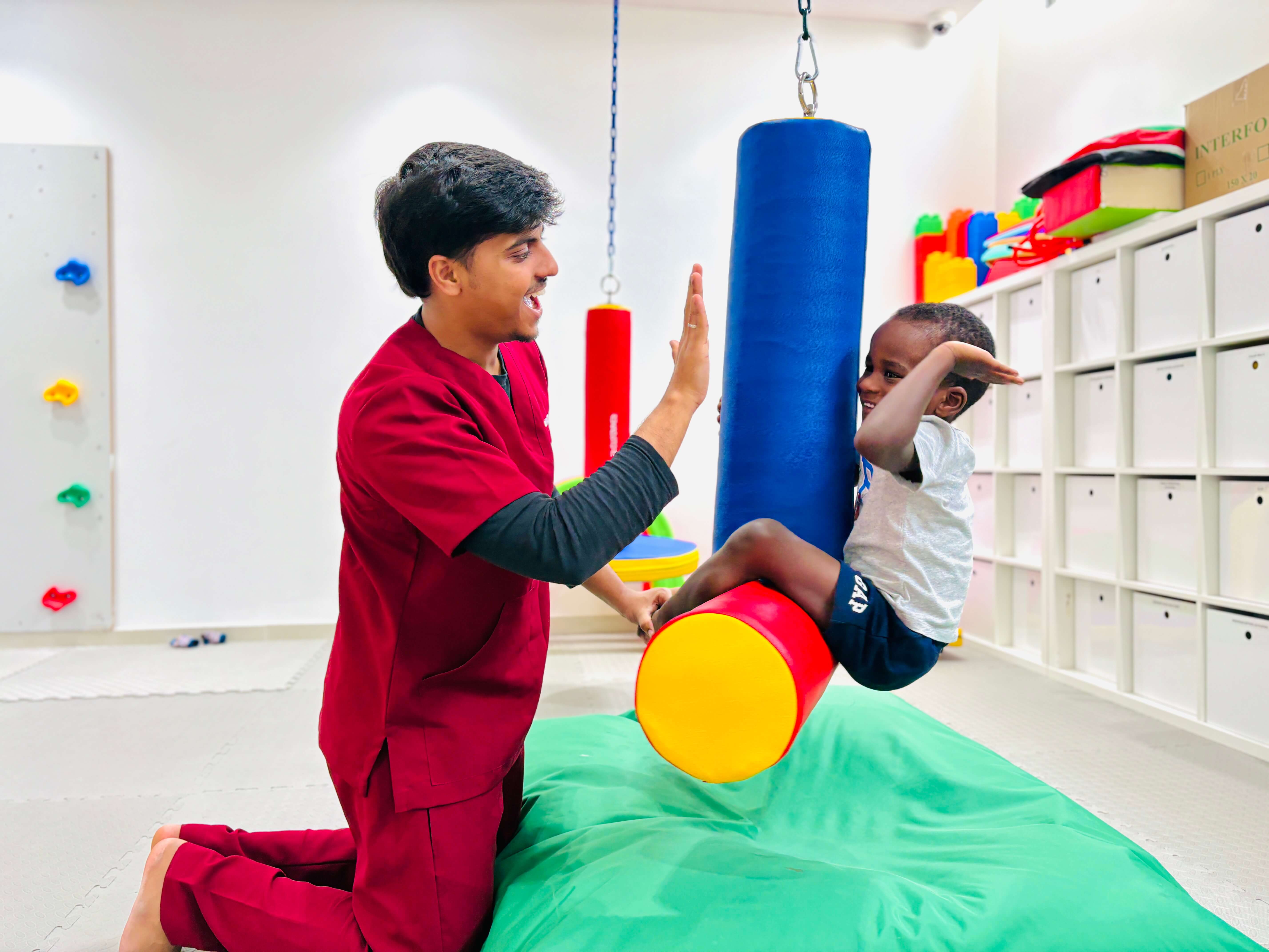 Therapist and child celebrating during a vestibular swing-bolster activity at Bridges Care Speech Therapy Center