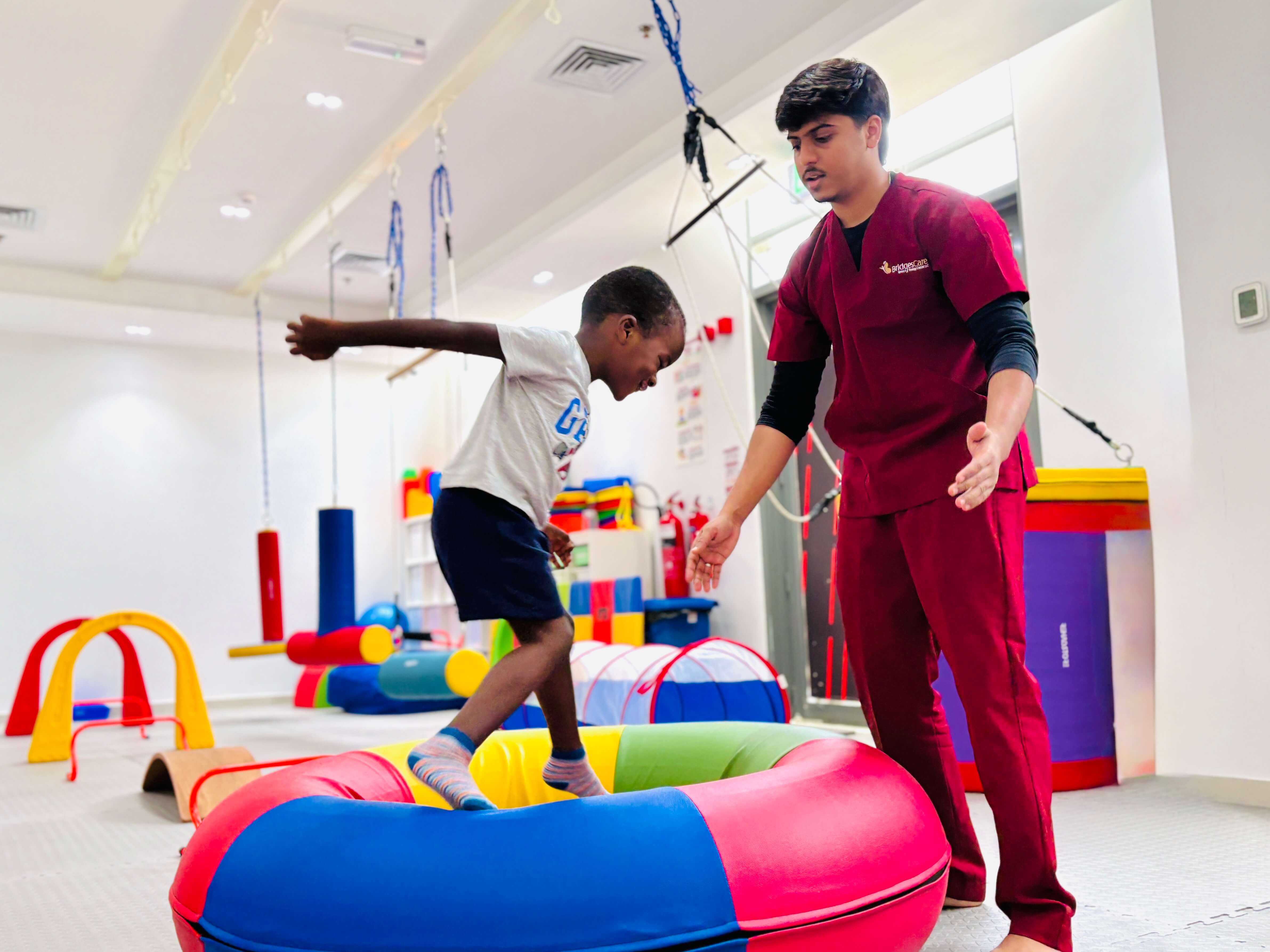 Child balancing on a colourful bolster with therapist support at Bridges Care Speech Therapy Center